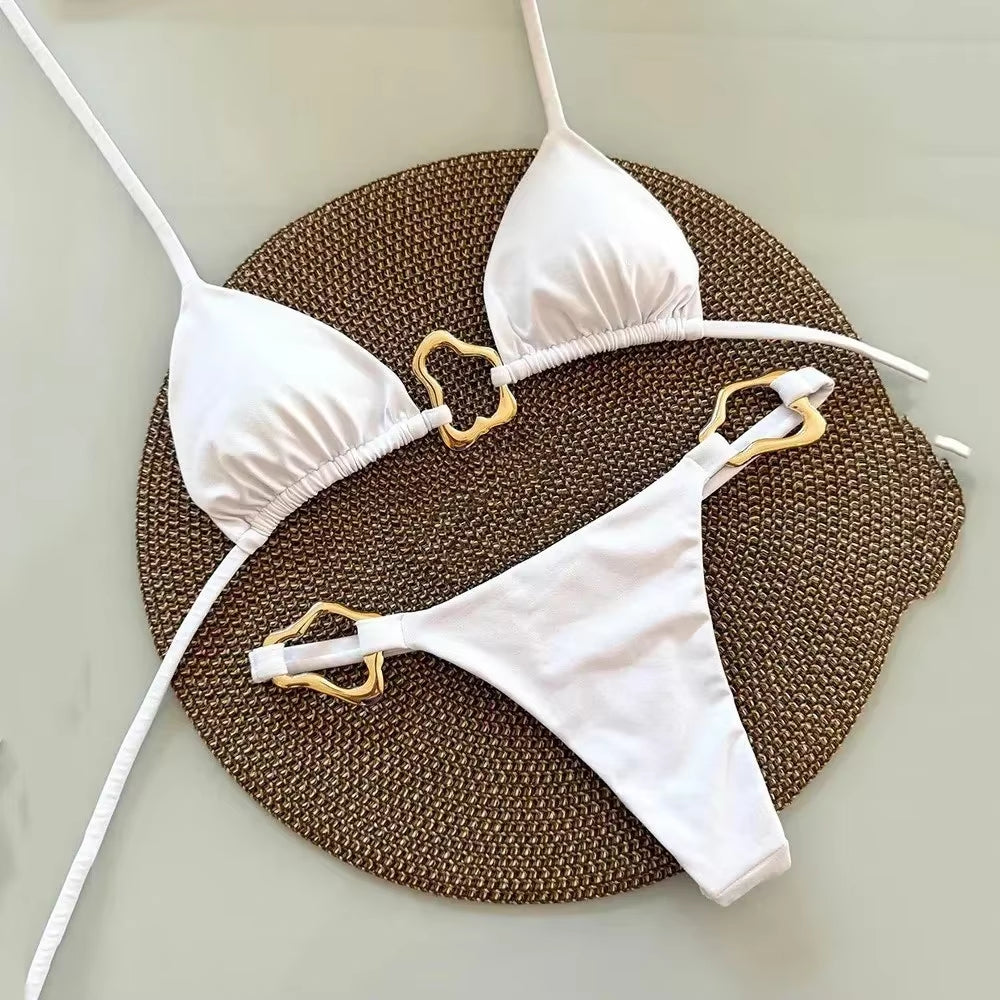 White halter triangle bikini set featuring elegant gold accents on the straps, resting on a woven placemat.