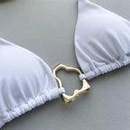 Close-up of a white bikini top featuring a gold decorative clasp, highlighting its elegant design.