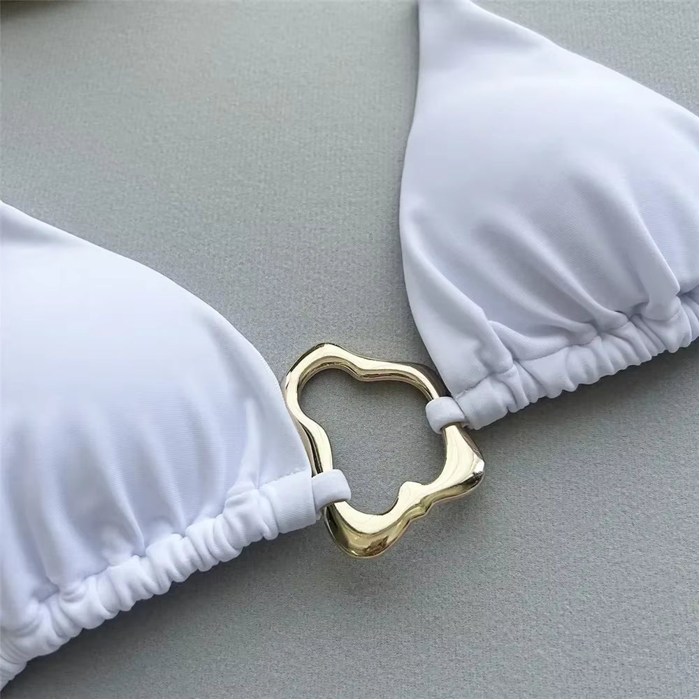 Close-up of a white bikini top featuring a gold decorative clasp, highlighting its elegant design.